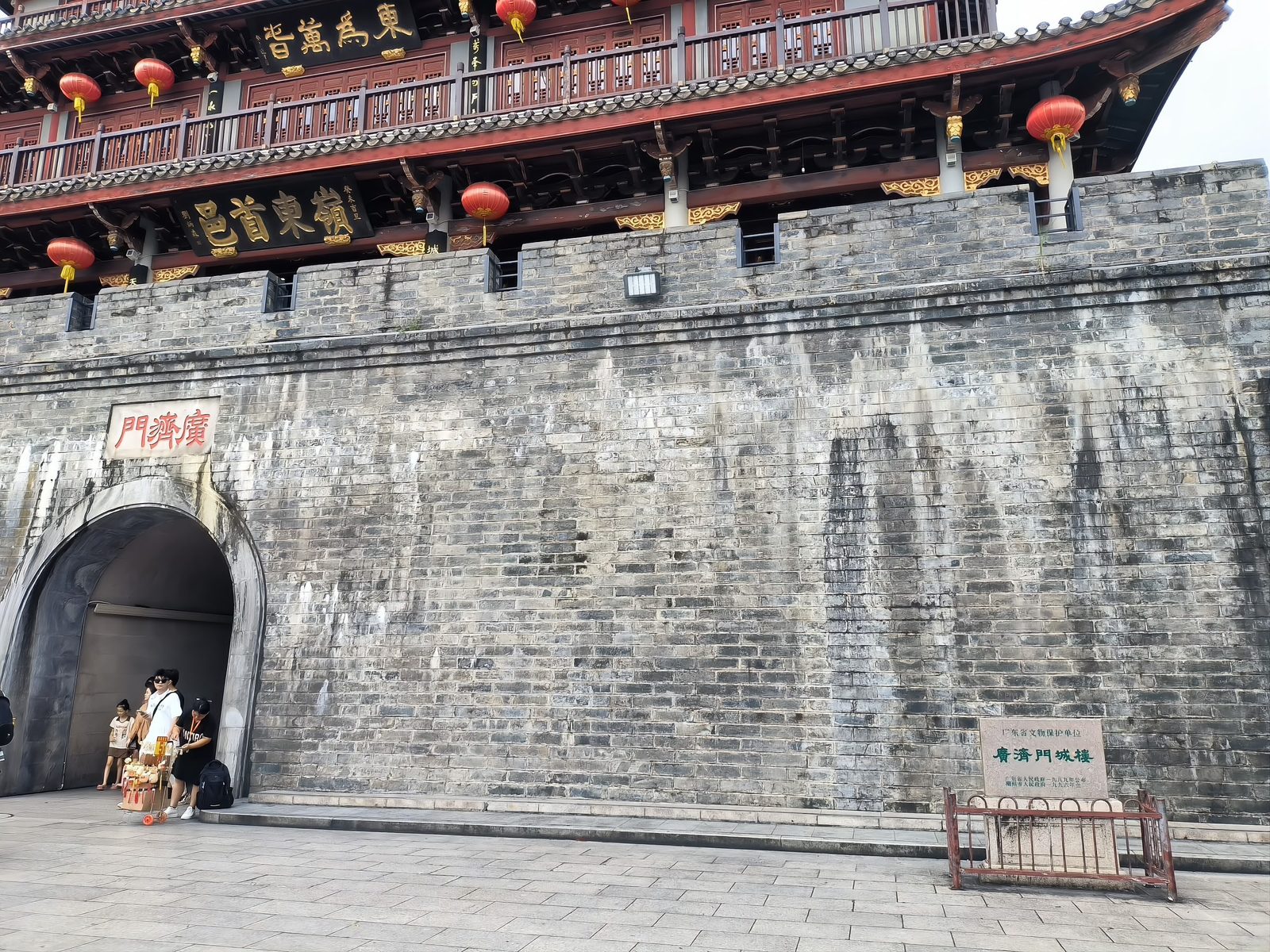 The Guangji Gate tower seen from below: grey brick ramparts, the arched gateway with its carved plaque, and three tiers of pavilions hung with red lanterns
