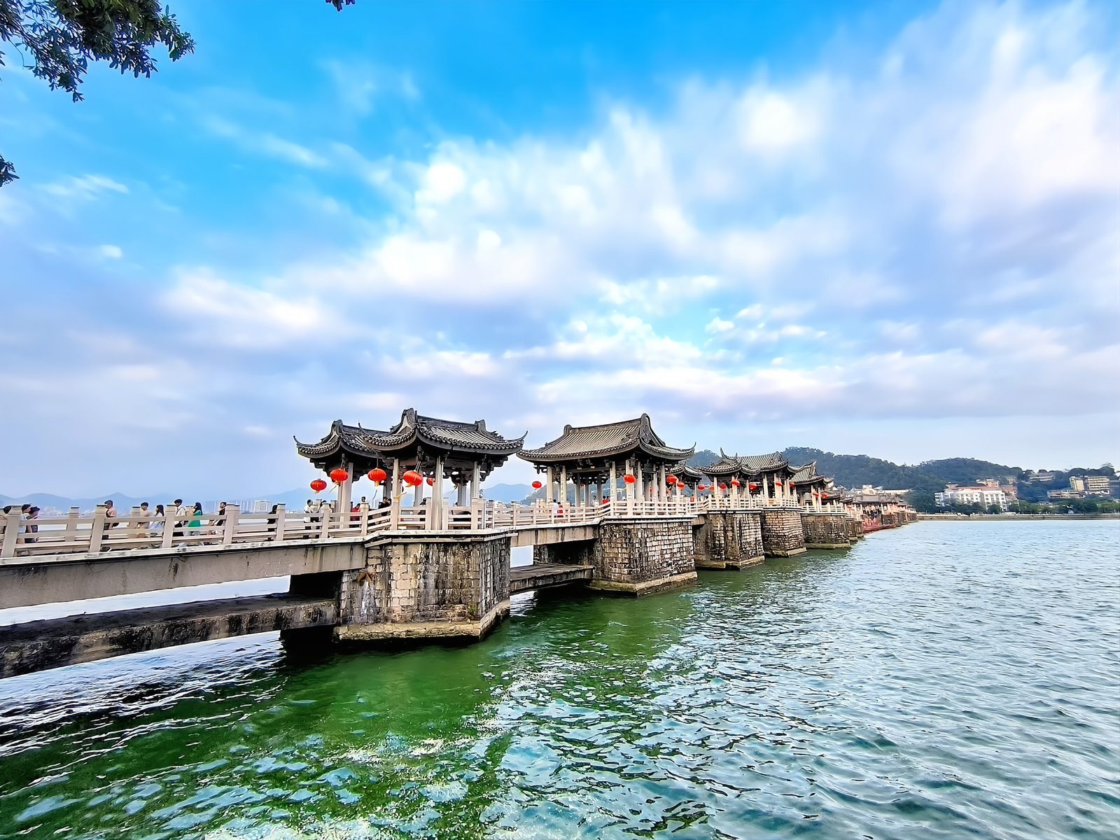 Guangji Bridge seen across the green water of the Han River, its stone piers and tiled pavilions running from bank to bank under a bright sky