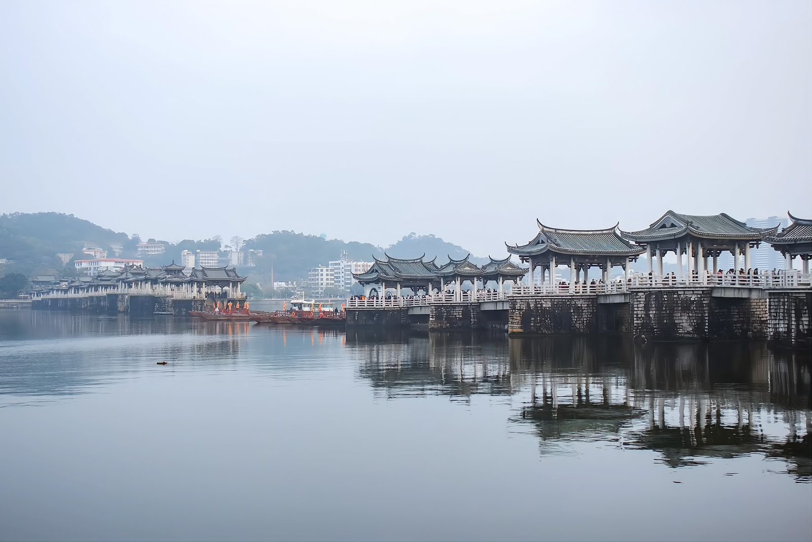 Guangji Bridge in early morning mist: stone piers and pavilions reflected in calm water, the shuttle boats gathered at the stone heads