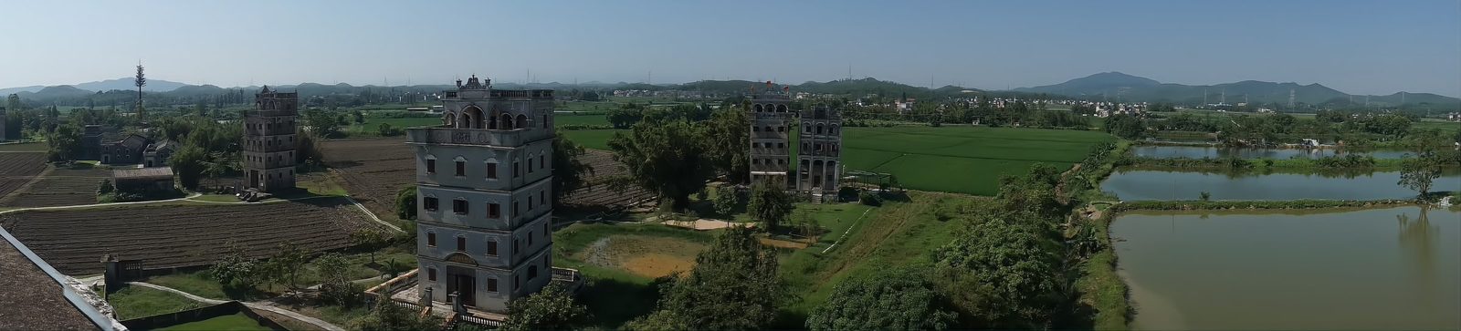 Panorama of Zili village in Kaiping: several fortified diaolou towers standing among rice paddies, fish ponds and green fields, with low hills on the horizon