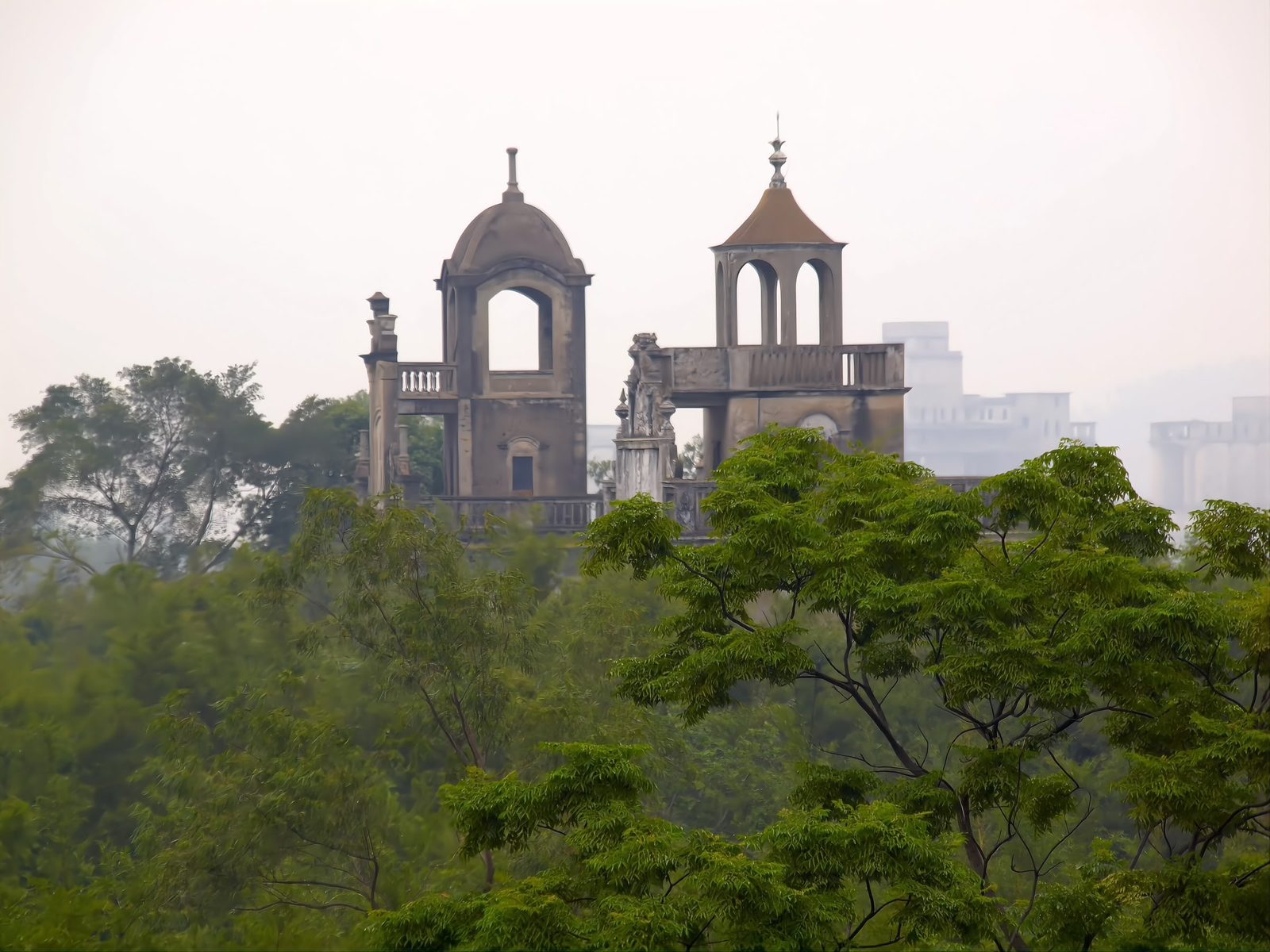 Diaolou towers rising out of dense green bamboo foliage in soft haze