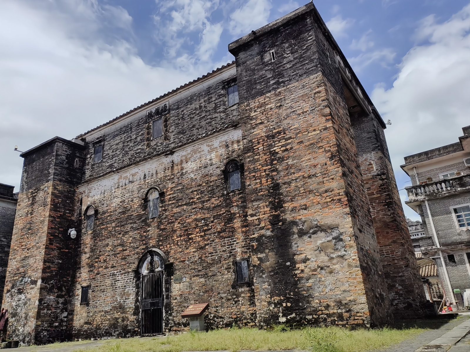 The Welcoming Dragon Tower, the oldest surviving diaolou: a dark weathered brick and stone tower with small windows and an arched doorway, blue sky behind