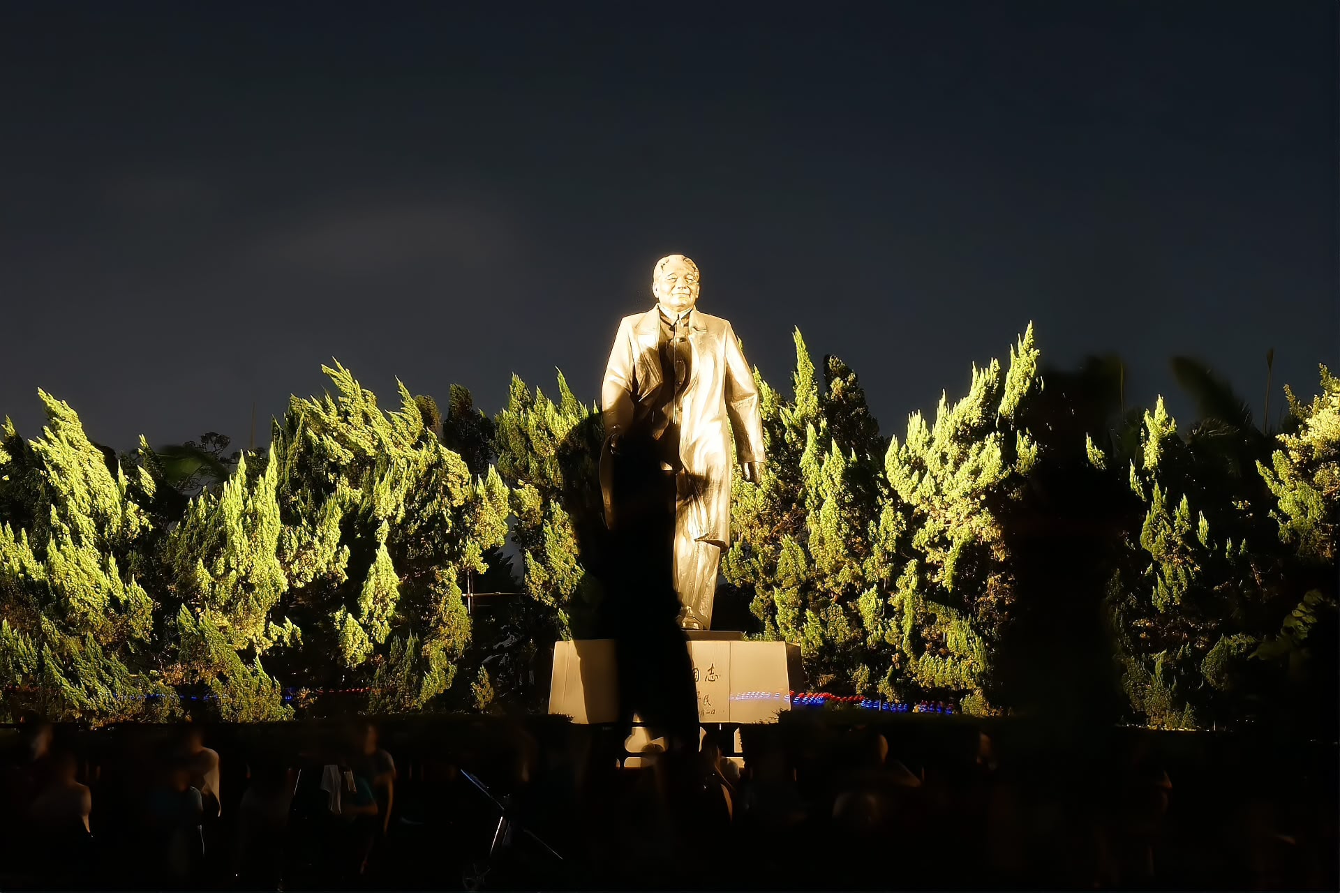 The bronze statue of Deng Xiaoping on the summit square of Lianhuashan Park at night, lit against the Shenzhen skyline