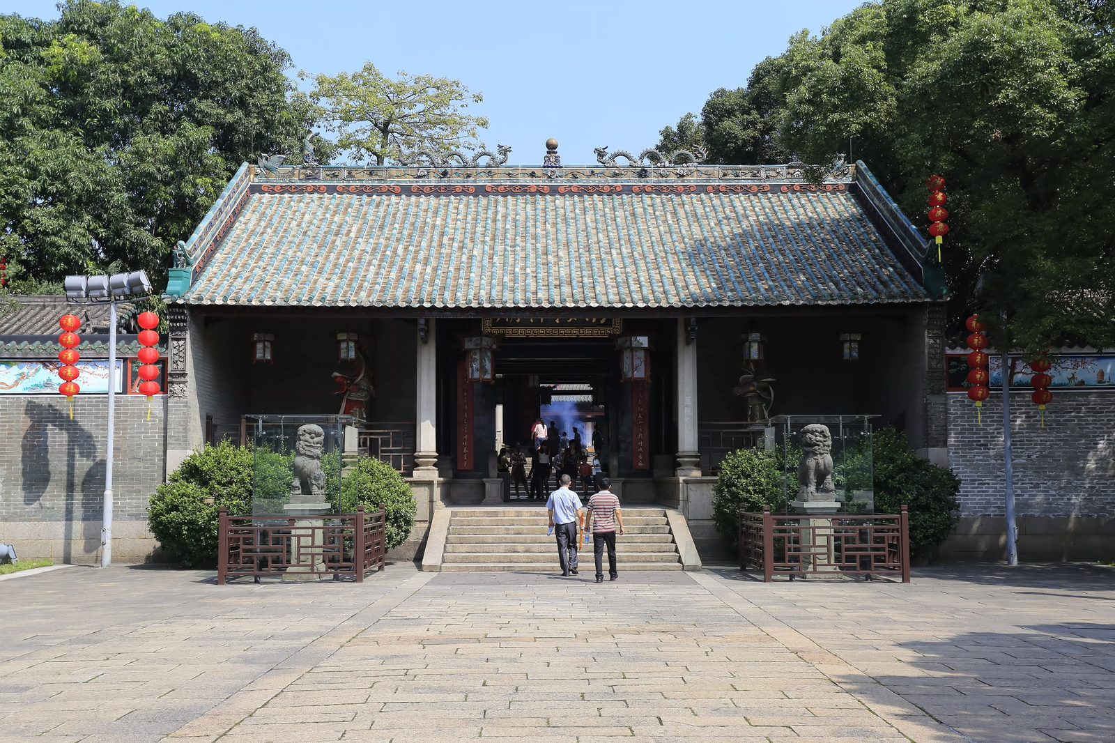 The first gate of Nanhai Temple: a grey-brick building under a green glazed tile roof with two dragons on the ridge, stone lions in glass cases flanking the steps, red lanterns at the eaves