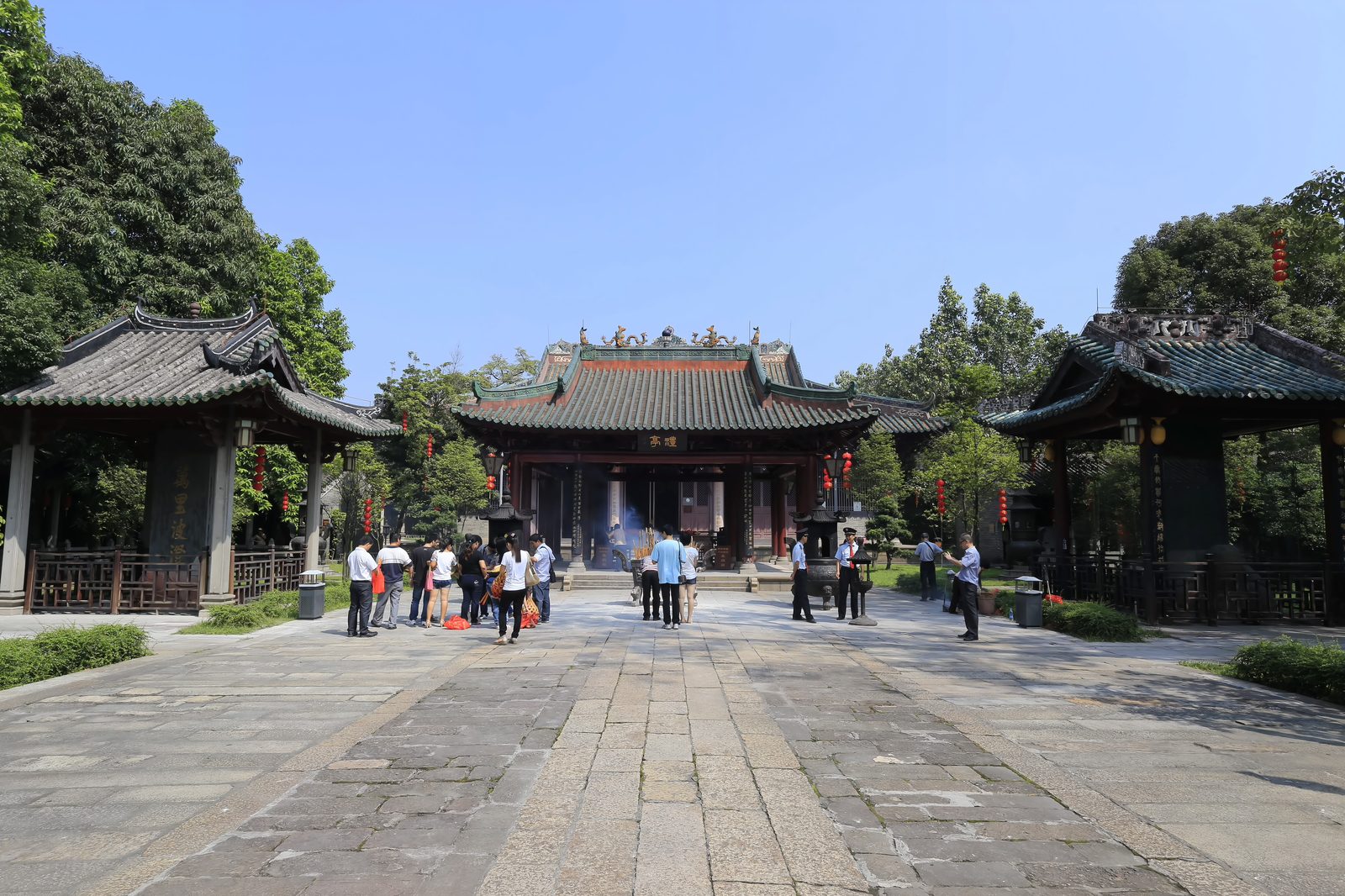 A wide granite courtyard at Nanhai Temple with the open ritual pavilion at its centre under a plaque reading Li Ting, flanked by two square stele pavilions, visitors crossing the stone