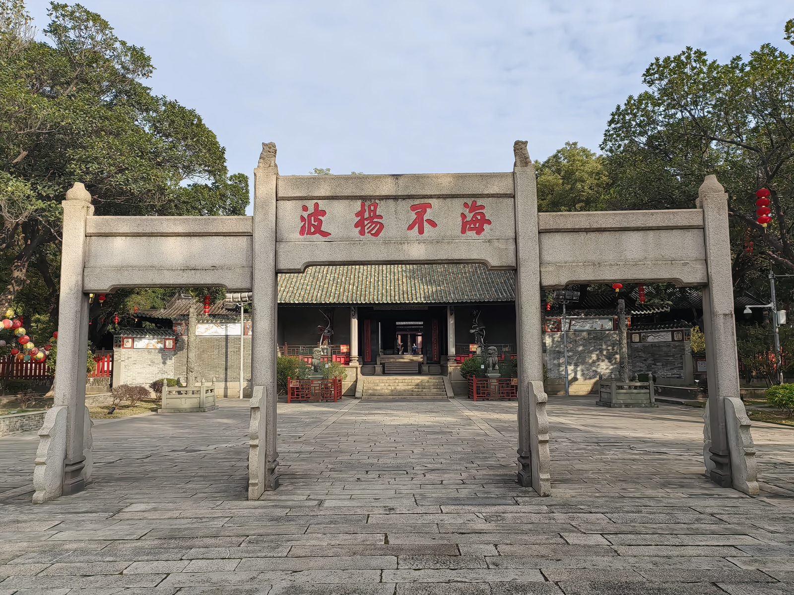 The granite archway of Nanhai Temple carrying four large red characters reading hai bu yang bo, the sea raises no waves, with the temple's first gate and green tiled roof behind