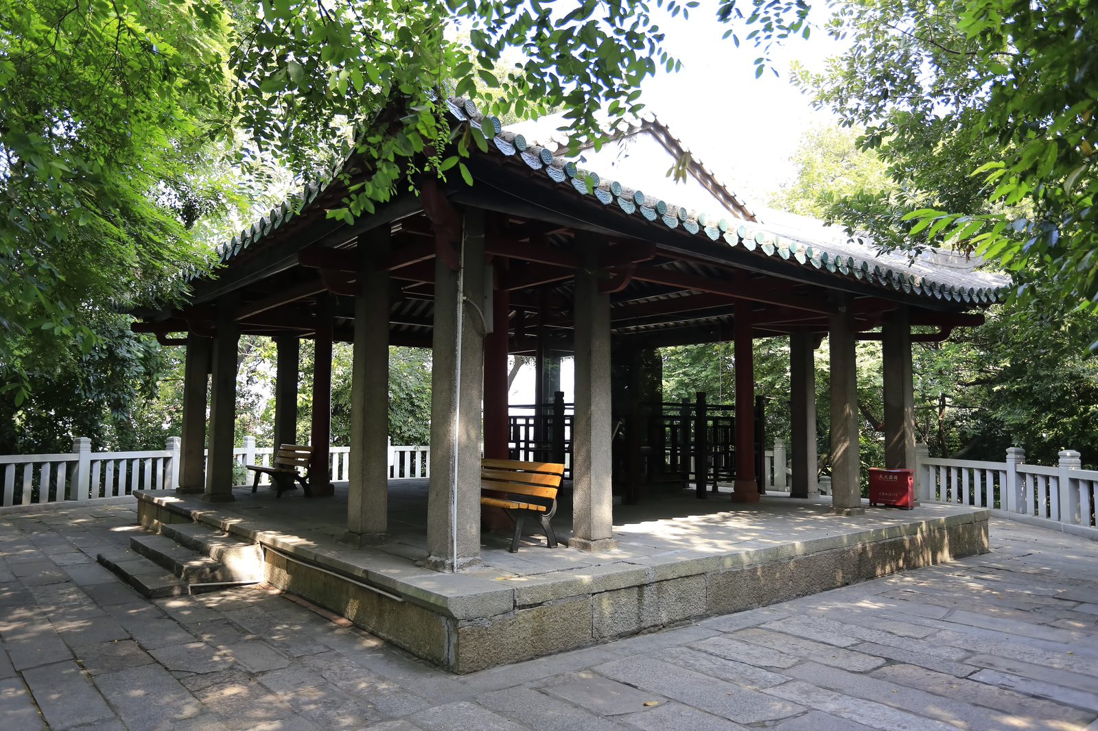 The Yuriting pavilion on Zhangqiu hill beside Nanhai Temple: an open pavilion of stone columns under a green tiled roof, standing on a stone terrace with white balustrades under dense trees