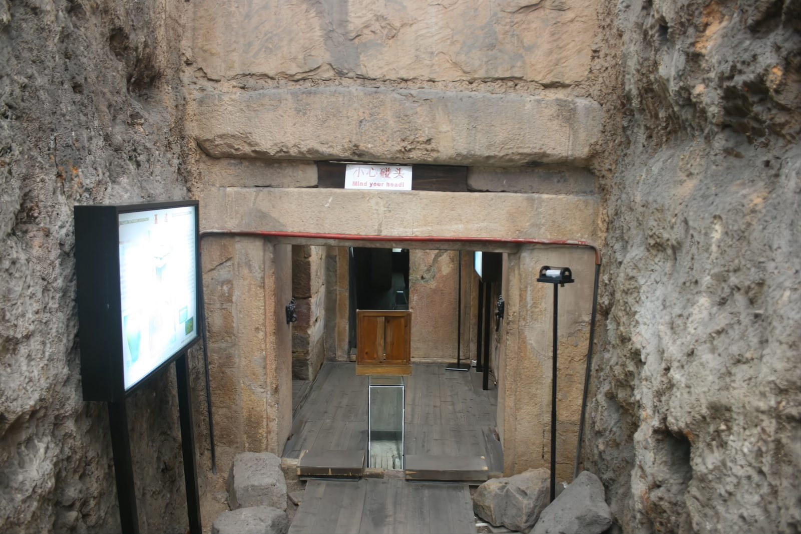 The stone entrance passage of the Nanyue King's Tomb, seen from inside the preserved chamber: massive red sandstone blocks framing the doorway, a lit display panel to one side, the shadowed rooms beyond