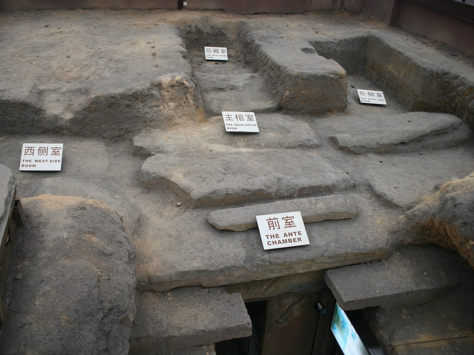 The excavated burial pit of the Nanyue King's Tomb seen from above: red sandstone chamber walls forming seven rooms around a central coffin chamber, with the modern visitor walkway along one side