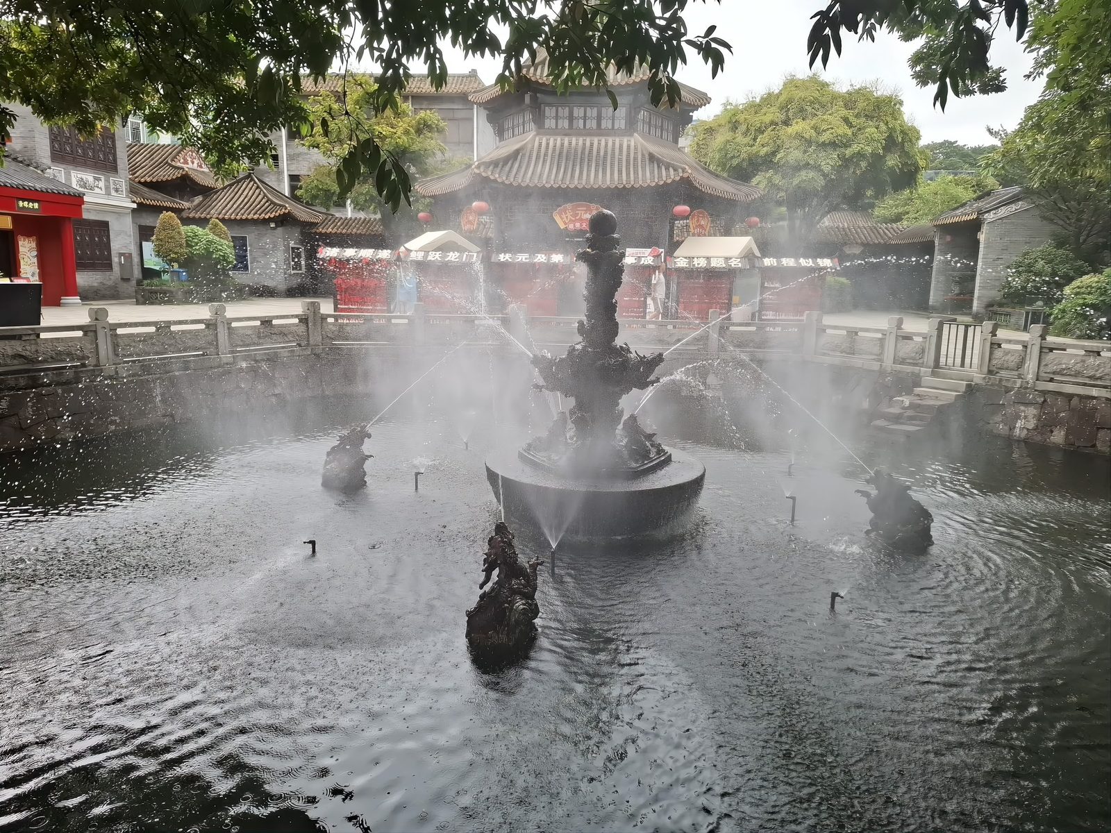 Qinghui Garden: a pond in the foreground with spray rising from a fountain, rockery and trees behind, and traditional Lingnan buildings at the water's edge