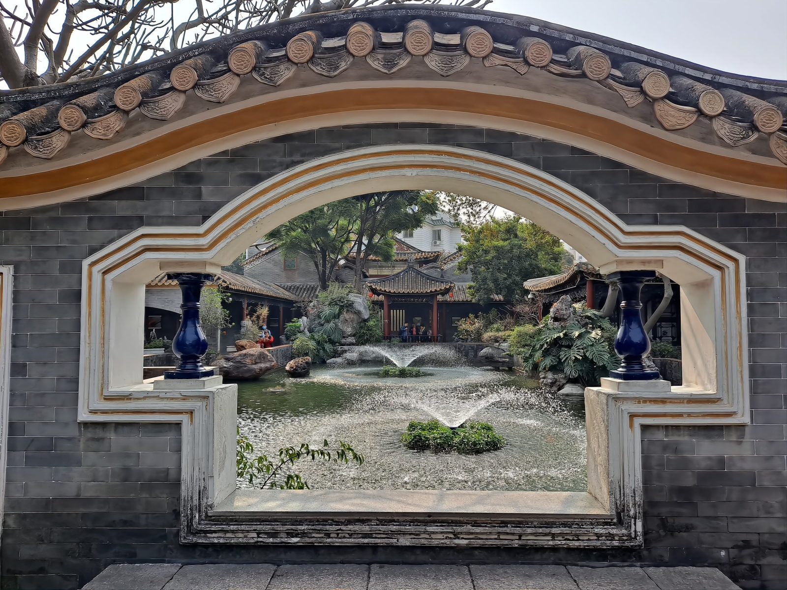 A circular moon gate in a grey brick wall, its frame full of planting, looking through to the green of the garden beyond