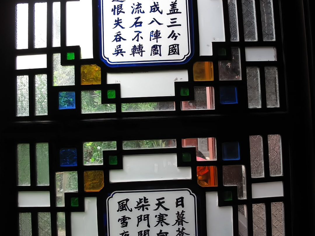 A traditional wooden window with coloured glass panes set in a timber lattice, a carved poem visible on the wooden frame beside it