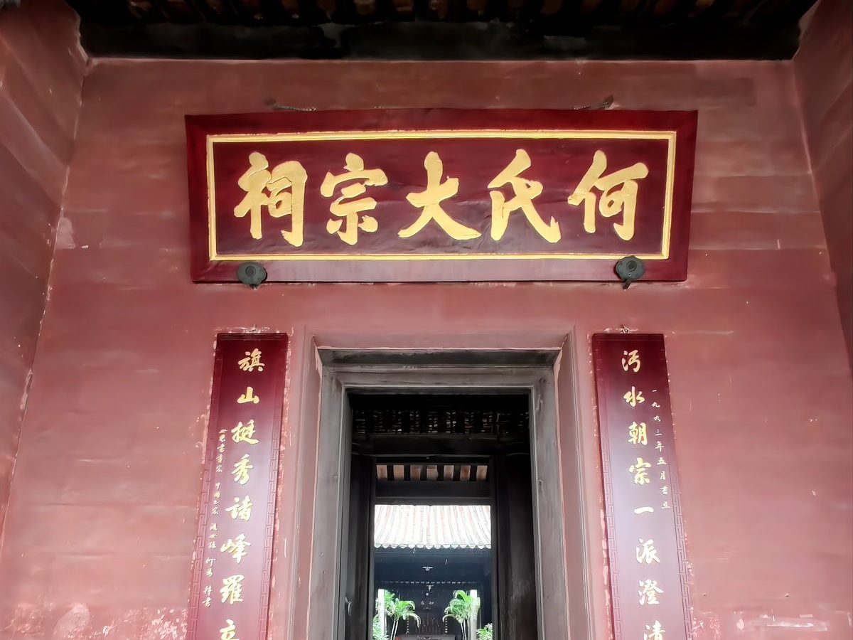 The entrance of the Liugeng Hall: a red wall with a gold plaque reading He Clan Ancestral Hall, flanked by red couplets, with open dark doors