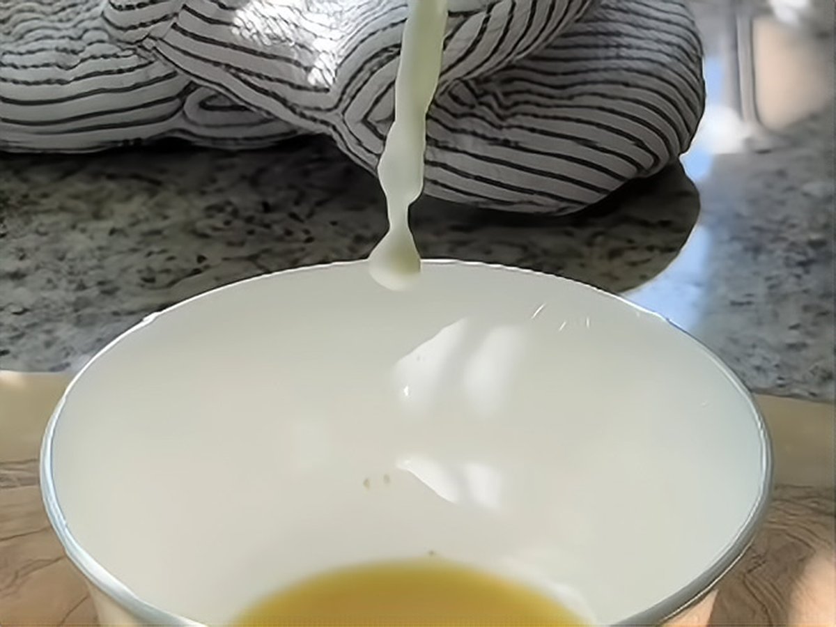 Hot milk poured in a thin stream into a white bowl holding a pool of golden ginger juice