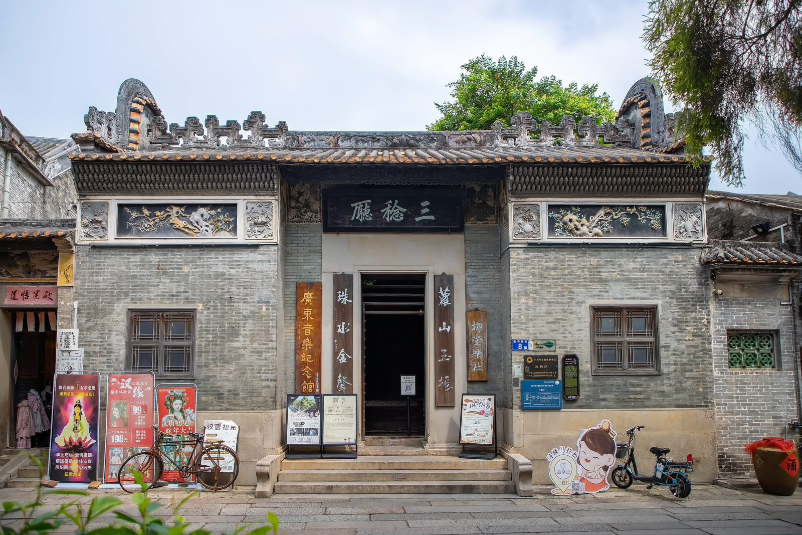 The Sanren Hall on Peaceful West Street: a grey-brick Lingnan house with tiled gables and stone carvings, its doorway hung with signage for the Guangdong Music Memorial Hall