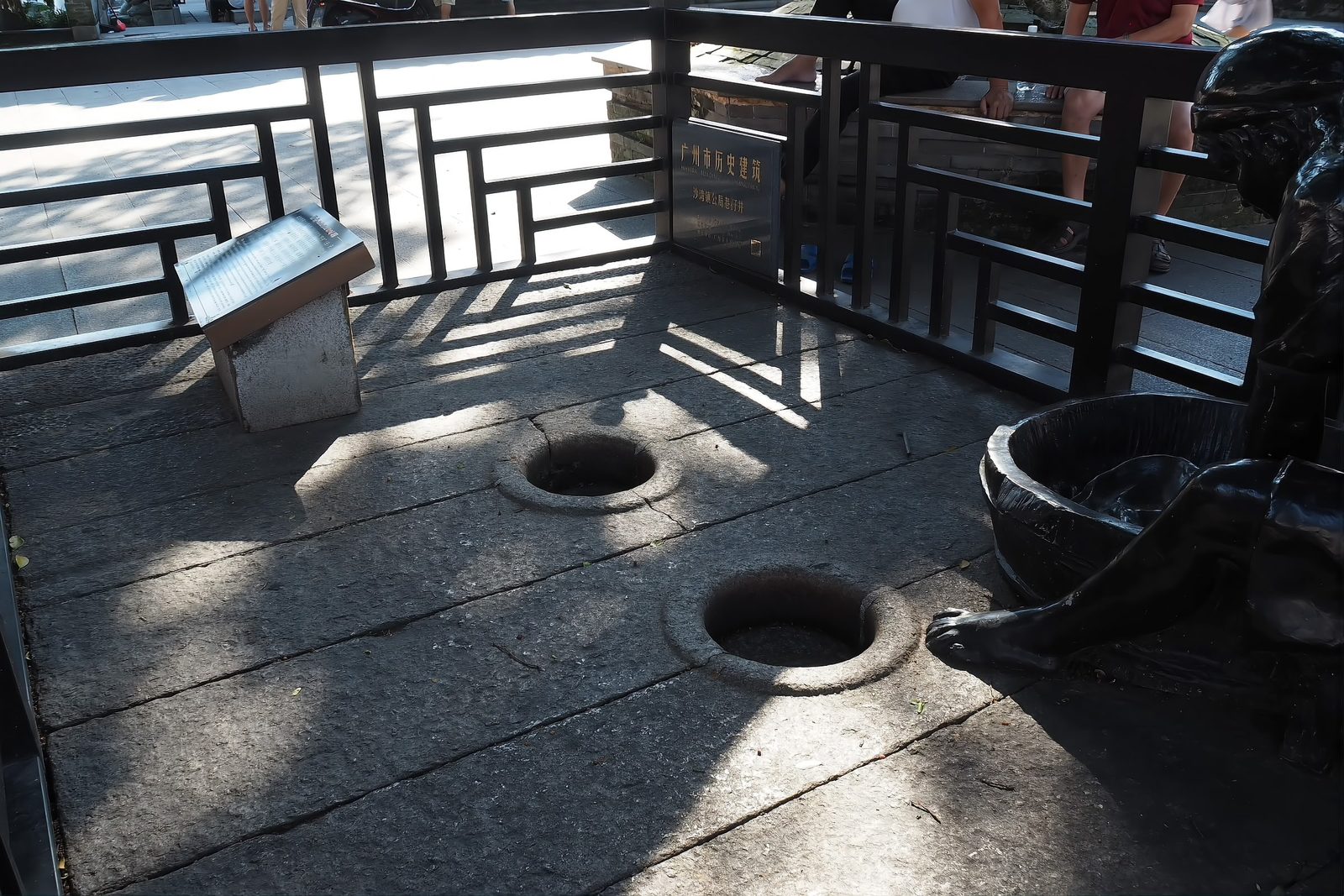 An old stone well with two round openings set in granite paving, with bronze figures of women washing beside it