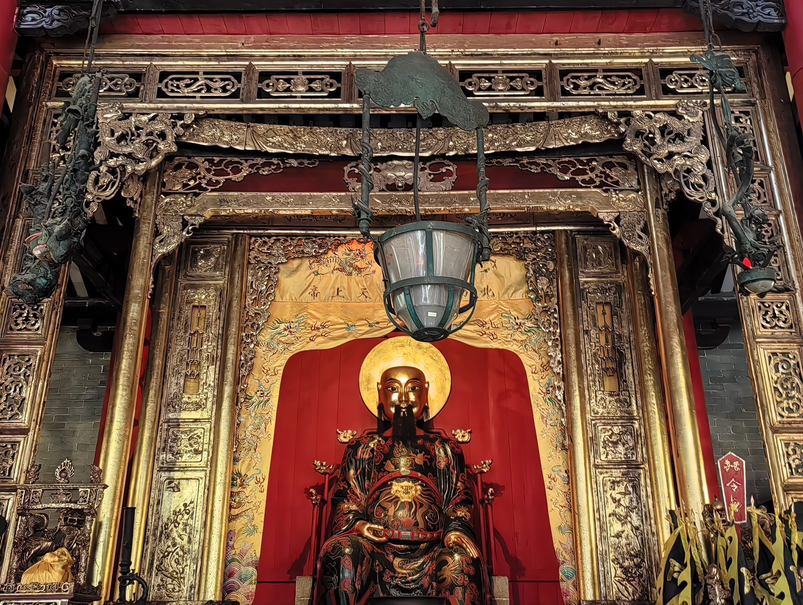 The gilt bronze statue of the Northern Emperor seated in a carved and gilded canopy inside the main hall of the Foshan Ancestral Temple, a lantern hanging in front