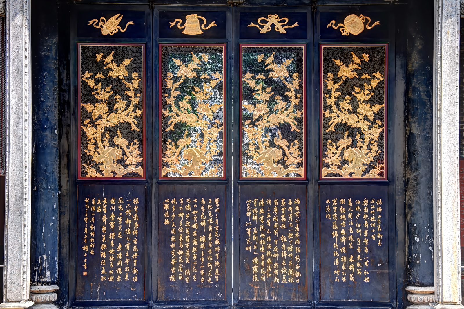 Four tall door panels of black lacquer with gilt: flowering branches and peacocks in gold relief above panels of gold calligraphy