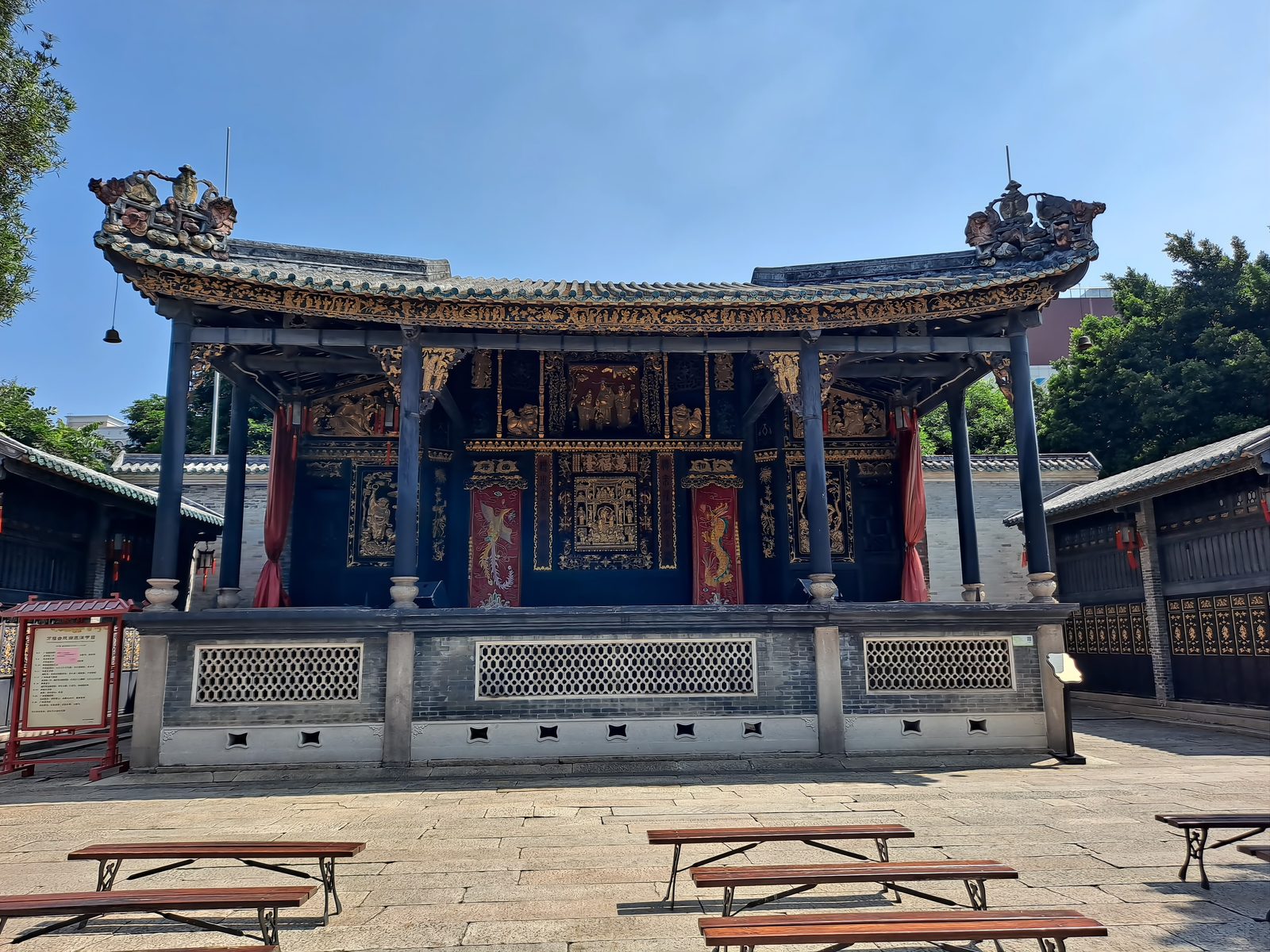 The Wanfu Stage of the Foshan Ancestral Temple: a wide timber stage of dark wood covered in gilt carving, red curtains at the sides, stone flagstones and wooden benches in front